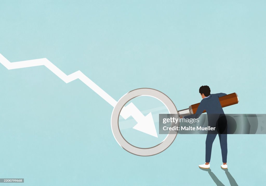 Businessman holding magnifying glass over descending chart arrow