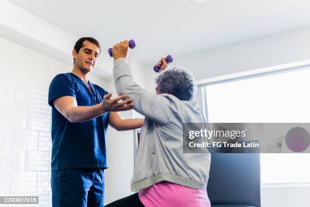 mid adult physical therapist helping patient during exercise with dumbbell - terapia ocupacional imagens e fotografias de stock