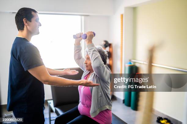 mid adult physical therapist helping patient during exercise with dumbbell - rehabilitation center stock pictures, royalty-free photos & images