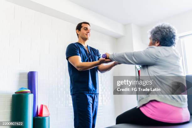 mid adult physical therapist helping patient during exercise with dumbbell - rehabilitation center stock pictures, royalty-free photos & images