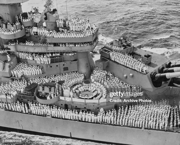 United States Navy personnel of the Iowa-class battleship USS Missouri mass on the main deck and superstructure of the battleship to observe the...