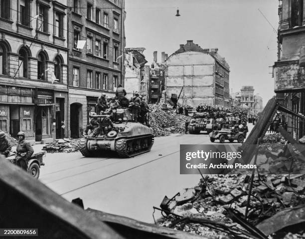 German civilians look on from windows waving white flags of surrender as an M4A1 Sherman leads a column of Sherman tanks from the 20th Armoured...