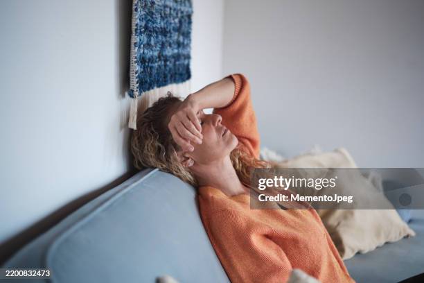 depressed woman at home, lying with eyes closed touching forehead, suffering from headache or migraine. middle-aged female sitting on sofa feeling down, sad and upset. menopause and your mental wellbeing - menopausa foto e immagini stock