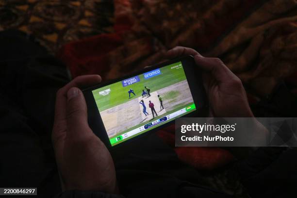 Man watches the live broadcast of the ICC Champions Trophy one-day international cricket match between Pakistan and India on a mobile phone in...