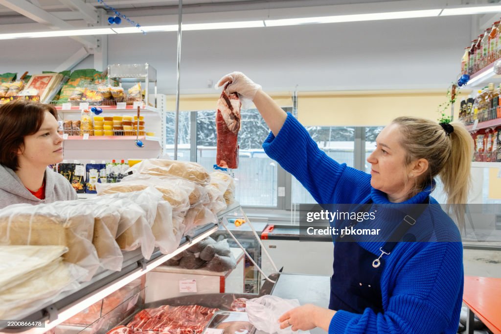 Professional guidance unfolds at supermarket meat section. Female butcher advises teen customer while presenting prime beef cuts