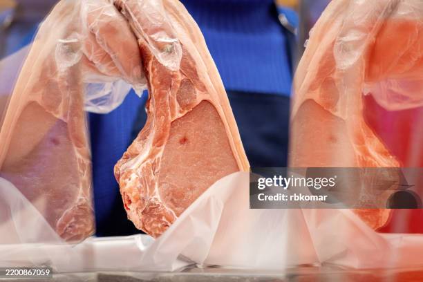 plastic-wrapped pork chops display quality marbling at butcher counter. fresh cuts rest on white paper with characteristic pink coloring - white butcher paper stock pictures, royalty-free photos & images