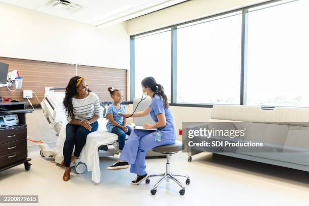 doctor examining a young girl with her mother in a hospital room - pediatric nurse stock pictures, royalty-free photos & images