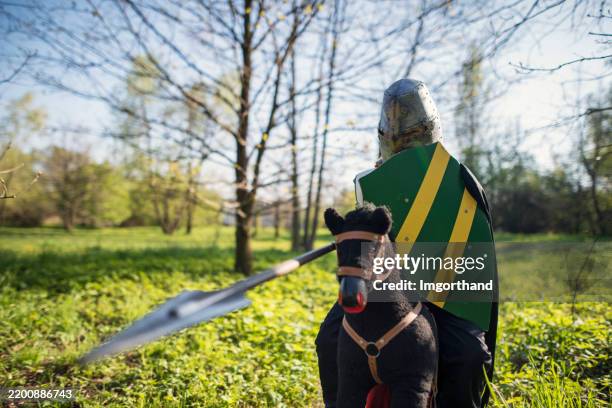 young boy dressed as a medieval knight riding a toy horse in the forest - fantasy battle stock pictures, royalty-free photos & images