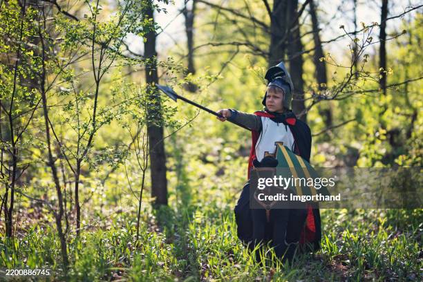 young boy dressed as a medieval knight riding a toy horse in the forest - ridder stockfoto's en -beelden