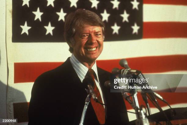 President Jimmy Carter smiling at a podium in front of an American flag, 1970s.