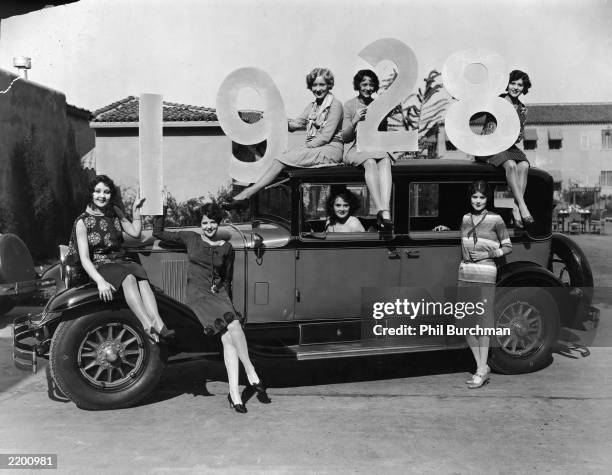 Group of female models pose around a new car in a promotional photo, holding large numbers for the year 1928. Rear : Gwen Lee, Sally Eilers, Dorothy...