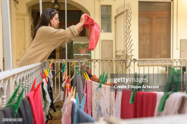 profile view of woman hanging laundry on a clothesline – italian balcony scene - drying stock pictures, royalty-free photos & images