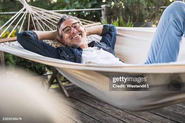 smiling man wearing eyeglasses relaxing in hammock - hängematte stock-fotos und bilder