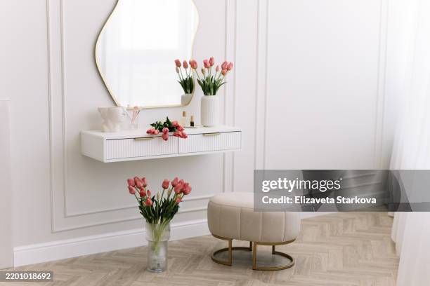 a corner of a modern elegant bedroom in a bright interior with a table and a mirror decorated with fresh flowers and tulips. dressing table for women - dressing table stock pictures, royalty-free photos & images