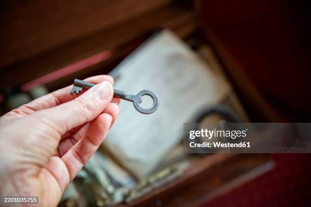 a woman holds an old key in her hand beside an old wooden box filled with family memories - legacy concept stock pictures, royalty-free photos & images