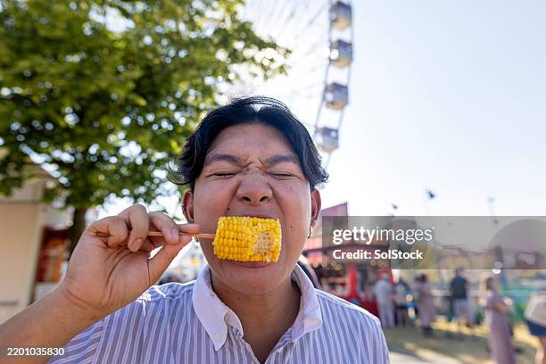 enjoying a corn on the cob at the fairground - espiga de milho imagens e fotografias de stock