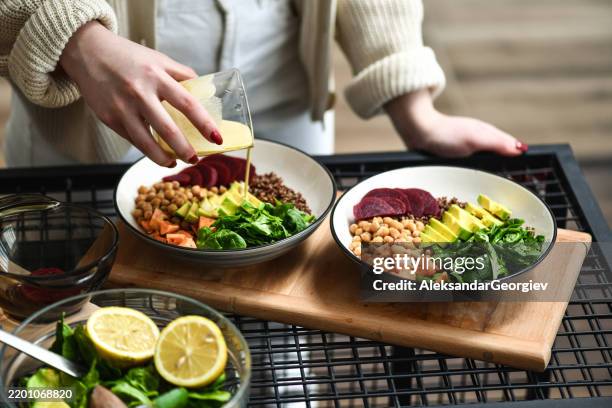 weiblich bereitet ästhetisch ansprechende salatschüsseln zu und fügt dressing hinzu, um die aromen miteinander zu verbinden - kichererbse stock-fotos und bilder