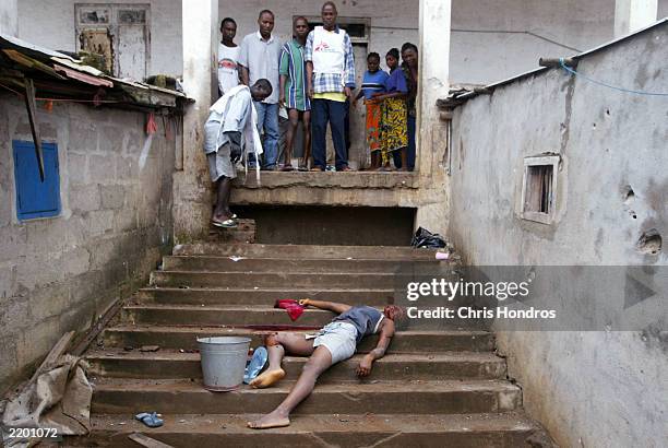 Shocked Liberians look on at the body of a woman who was killed by a shell while gathering water July 25, 2003 in Monrovia, Liberia. A fresh round of...