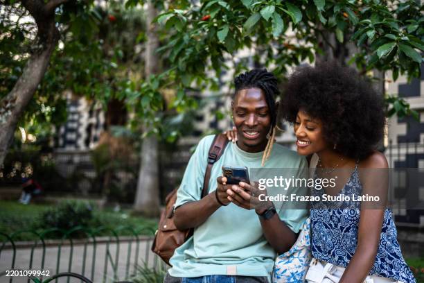 pareja joven o amigos hablando y usando el teléfono móvil al aire libre - afrocaribeño fotografías e imágenes de stock