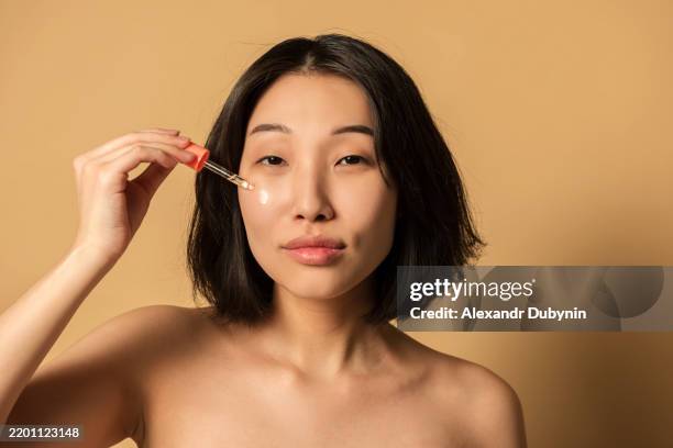 beauty portrait of asian woman dripping serum on her face for moisturizing skin studio shot - retinol stock pictures, royalty-free photos & images