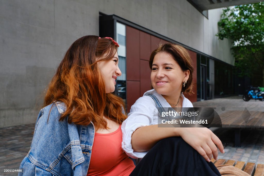 Happy lesbian couple sitting on bench in front of building