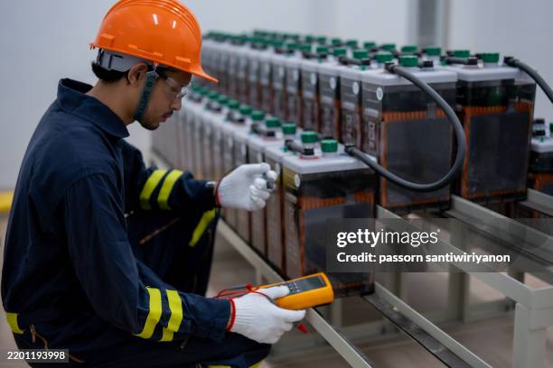 technician in orange helmet tests battery systems with multimeter, ensuring safety and efficiency in modern facility - osha hazard communication pictogram stock pictures, royalty-free photos & images