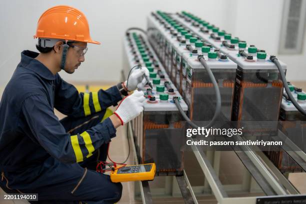 technician working on battery maintenance with multimeter in industrial setting. safety gear includes helmet and gloves, ensuring secure environment - battery manufacturing stock pictures, royalty-free photos & images