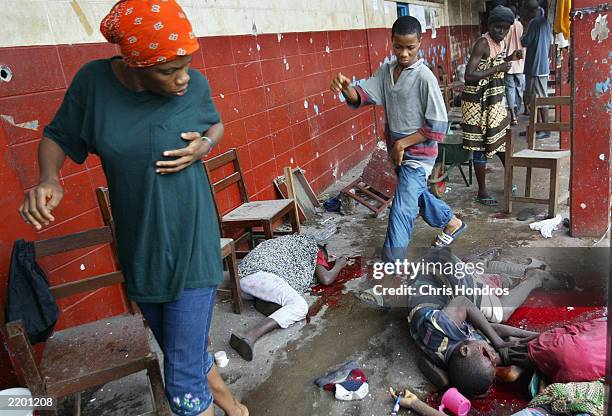 Shocked Liberians walk through the remains of shelling victims at the high school, where hundreds of refugees have been living, minutes after they...