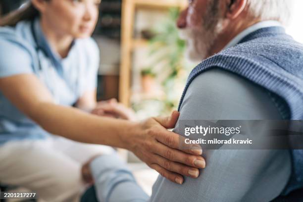 nurse comforting elderly patient by holding his shoulder - hand shoulder stock pictures, royalty-free photos & images