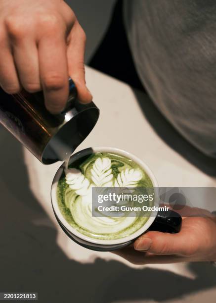 barista pouring steamed milk into a cup of matcha latte creating latte art, green tea beverage with creamy frothy texture, artistic coffee shop preparation, healthy and trendy drink concept - matcha stockfoto's en -beelden