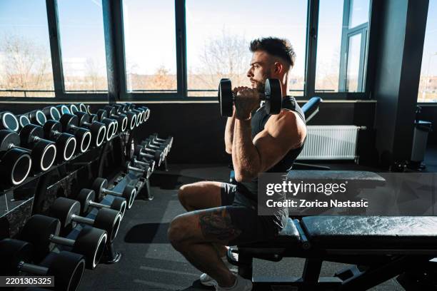 joven construyendo fuerza con mancuernas en el banco - entrenamiento de fuerza fotografías e imágenes de stock