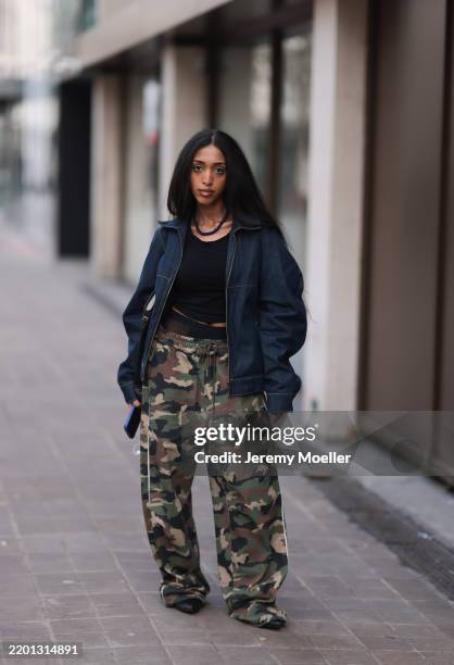 Fashion Week Guest seen wearing a black top, blue denim jeans jacket, camouflage pants, big golden creols and a black necklace chain and leather...