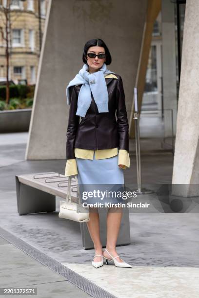Amalie Gassmann wears Toteme shoes, DeMellier bag, Mithridate skirt, shirt, jacket and jumper and black sunglasses during London Fashion Week...