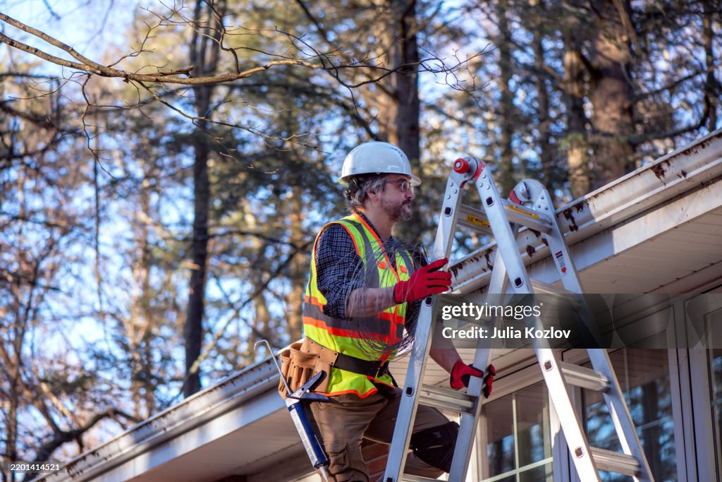 ヘルメット、反射ベスト、防水、家の外観などの安全装備を身に着けている成熟した労働者。はしごの請負業者は、住宅の屋根のメンテナンスを行います。
