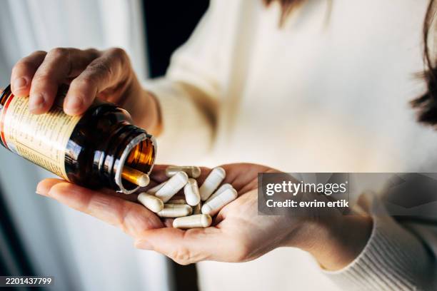 femme prenant des pilules de vitamines dans une bouteille - complément vitaminé photos et images de collection