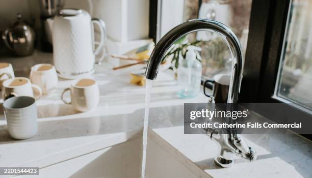 a running tap in front of a kettle and mugs - eau courante photos et images de collection