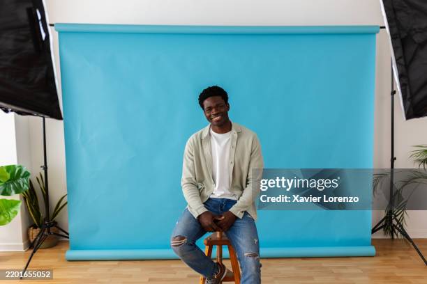 young male model posing in studio with blue backdrop - stool stock pictures, royalty-free photos & images