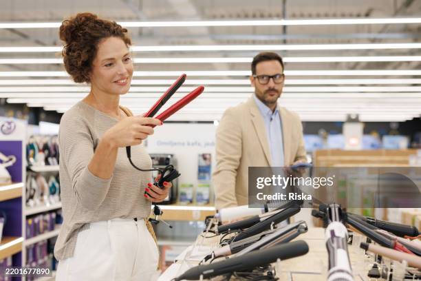 a woman examining a hair straightener while her husband looks disapprovingly - haar straighten stockfoto's en -beelden