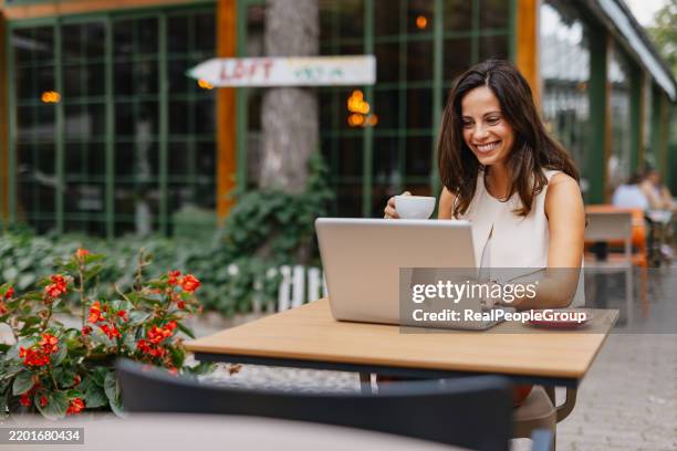 businesswoman drinking coffee and working on laptop at outdoor cafe - digital nomad stock pictures, royalty-free photos & images