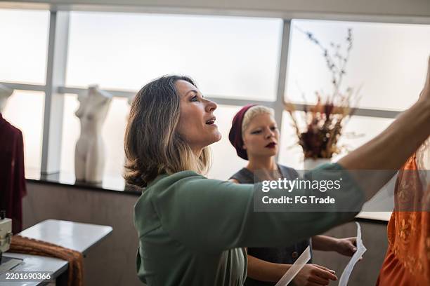 créatrice de mode mature discutant avec une assistante dans son atelier - industrie de la mode photos et images de collection