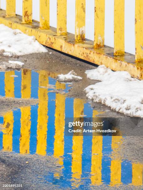 bright reflections of a yellow barrier dance across the waterlogged pavement on a chilly winter day - puddle stock pictures, royalty-free photos & images