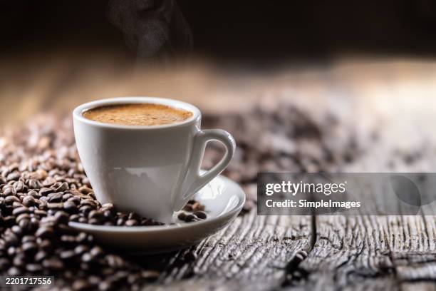 cup of black coffee with coffee beans on old wooden table - taza de café fotografías e imágenes de stock