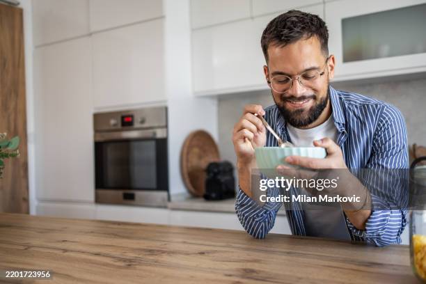 man enjoying a bowl of cereal for breakfast in his kitchen - breakfast cereal stock pictures, royalty-free photos & images