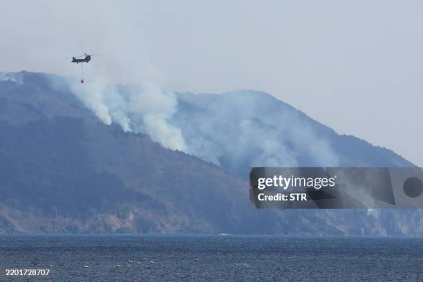 Helicopter is pictured as smoke rises due to a wildfire on a mountainside near the city of Ofunato, Iwate Prefecture on February 28, 2025. At least...