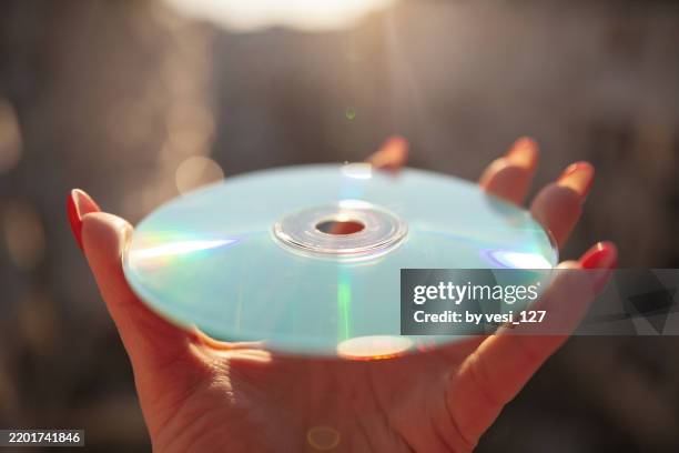a woman's hand with red manicure holding an old compact disc against a blurred background on a sunny day, copy space - old cd stock pictures, royalty-free photos & images