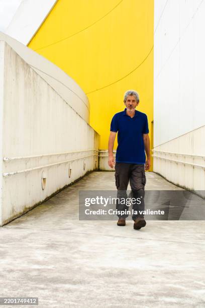mature man walking in a modern architectural space with yellow wall - vida sencilla fotografías e imágenes de stock
