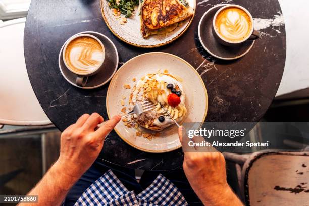 man eating pancakes with youghurt and fresh berries at a cafe, personal perspective directly above view - desayuno fotografías e imágenes de stock
