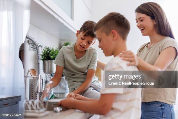 mother watching her two sons washing dishes in the kitchen - chores stock pictures, royalty-free photos & images