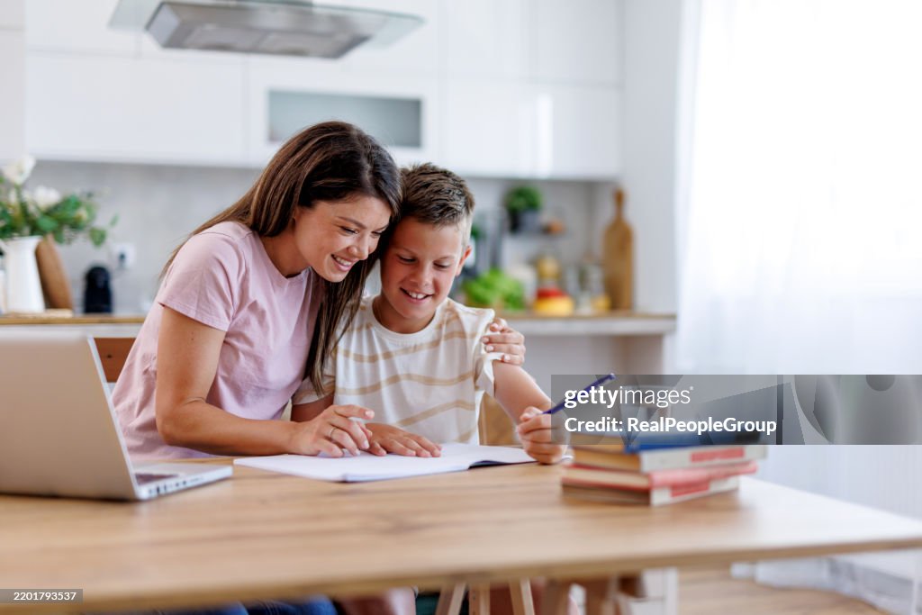 Mother helping son with homework at home kitchen table