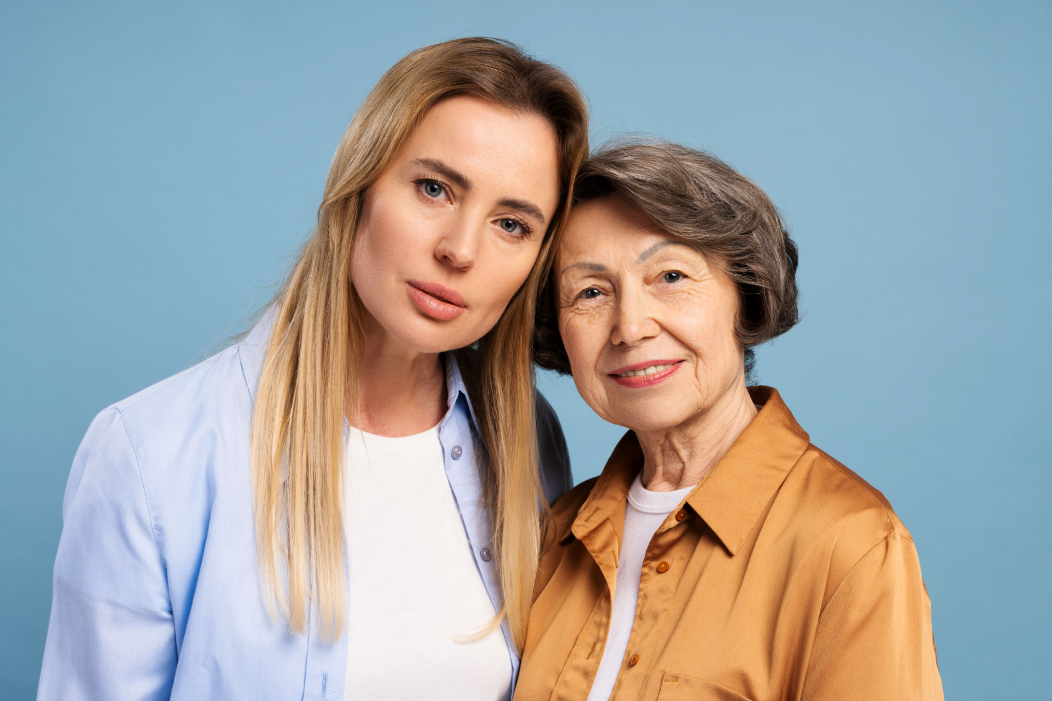Happy senior mother and adult daughter posing together on blue background Happy senior mother and adult daughter posing together on blue background